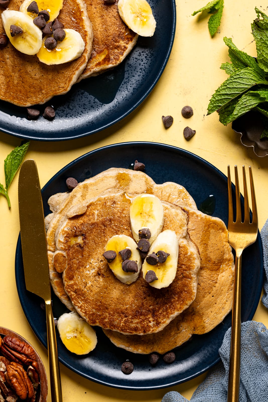 Pancakes on a blue plate with sliced bananas and chocolate chips and a knife + fork.