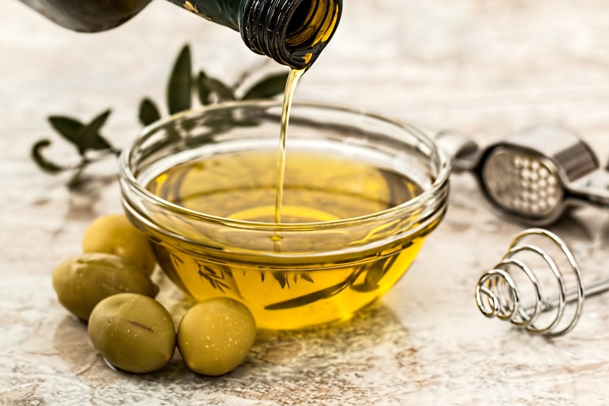 Jar pouring olive oil into a small glass bowl