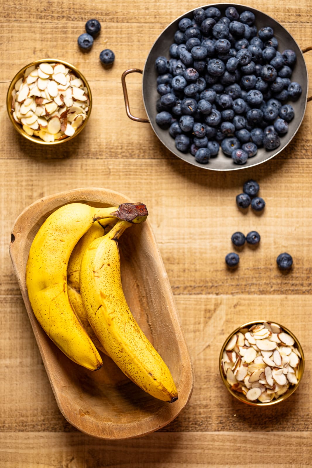 Bananas, blueberries, and almond slices on a brown wood table.