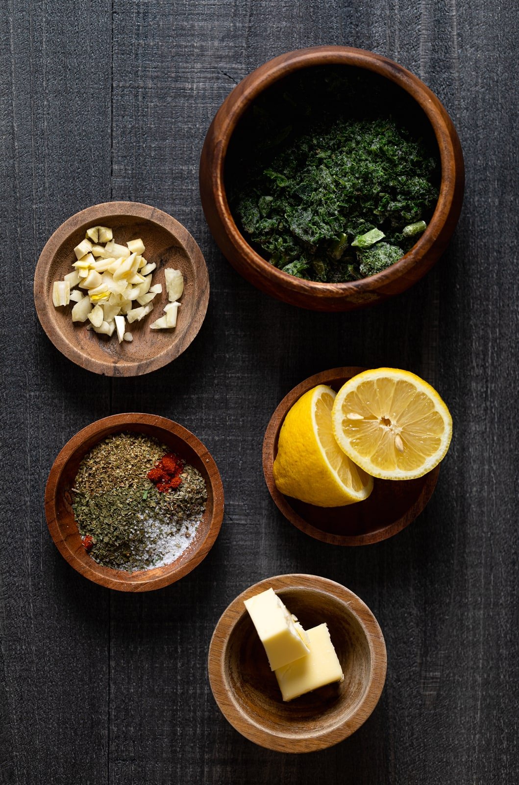 Wooden bowls of ingredients for Creamy Lemon and Herb Parmesan Chicken including garlic, lemon, and butter