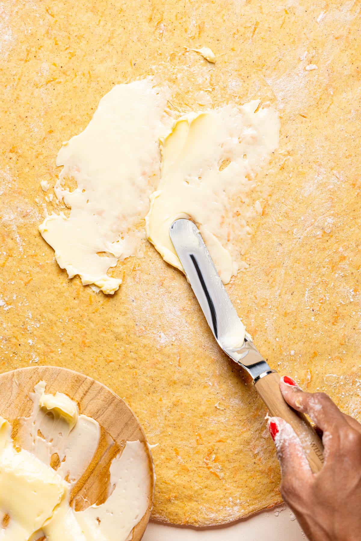 Knife spreading butter on flattened dough
