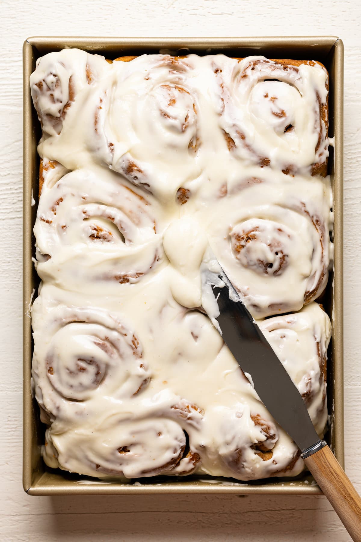 Knife spreading frosting on Southern-Style Carrot Cake Cinnamon Rolls