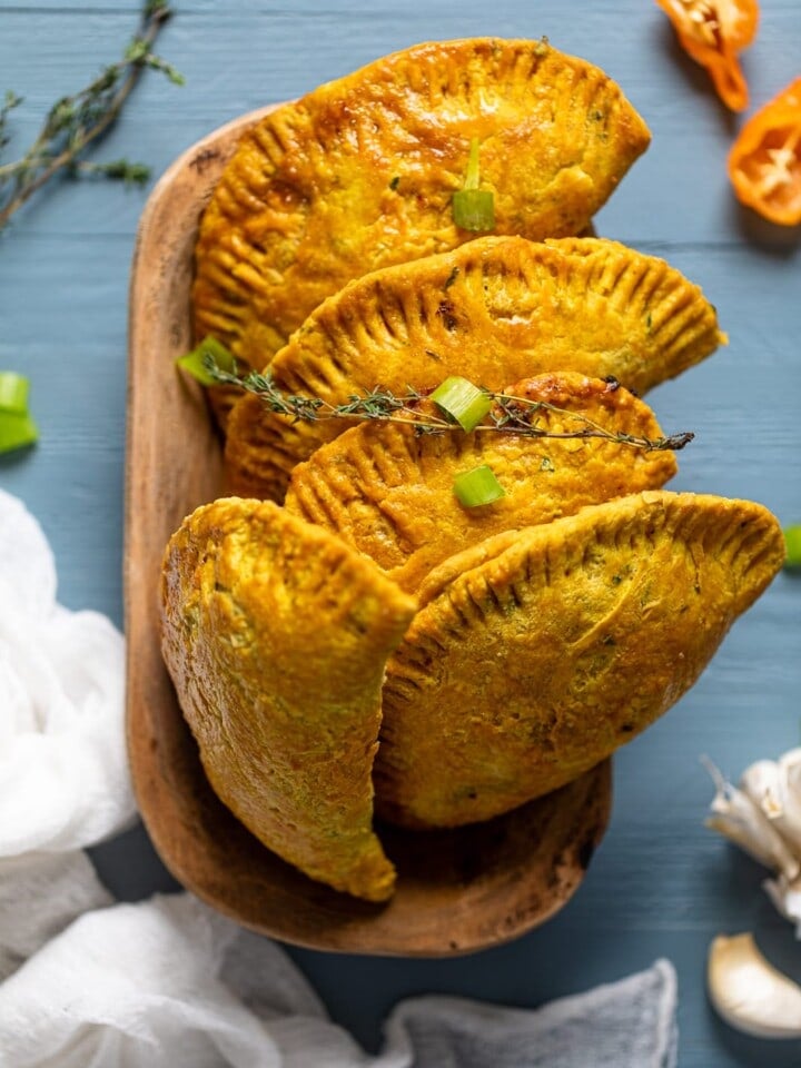 Five Spicy Jamaican Beef Patties standing up in a wooden bowl