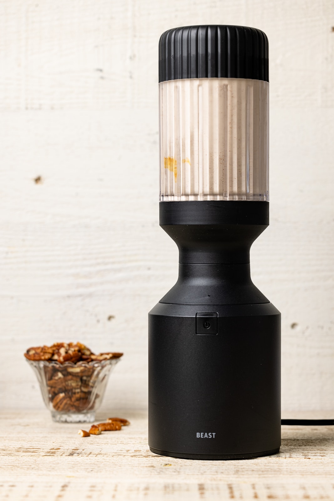 Milkshake in a black blender with a bowl of chopped pecans.