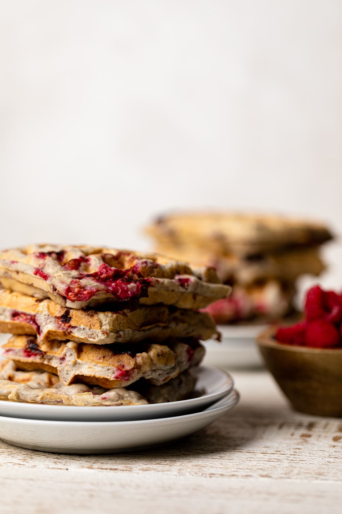 Stack of Raspberry Pecan Vegan Waffles next to a wooden bowl of raspberries