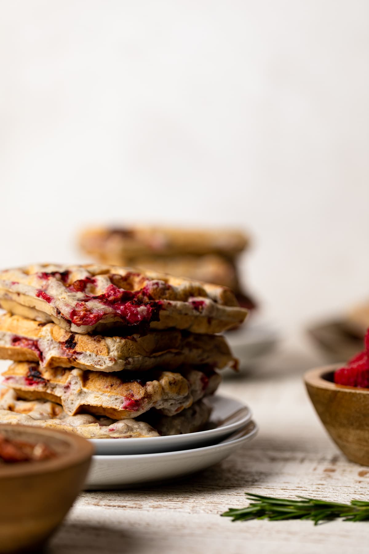 Stack of Raspberry Pecan Vegan Waffles on two small, stacked plates next to a wooden bowl of raspberries