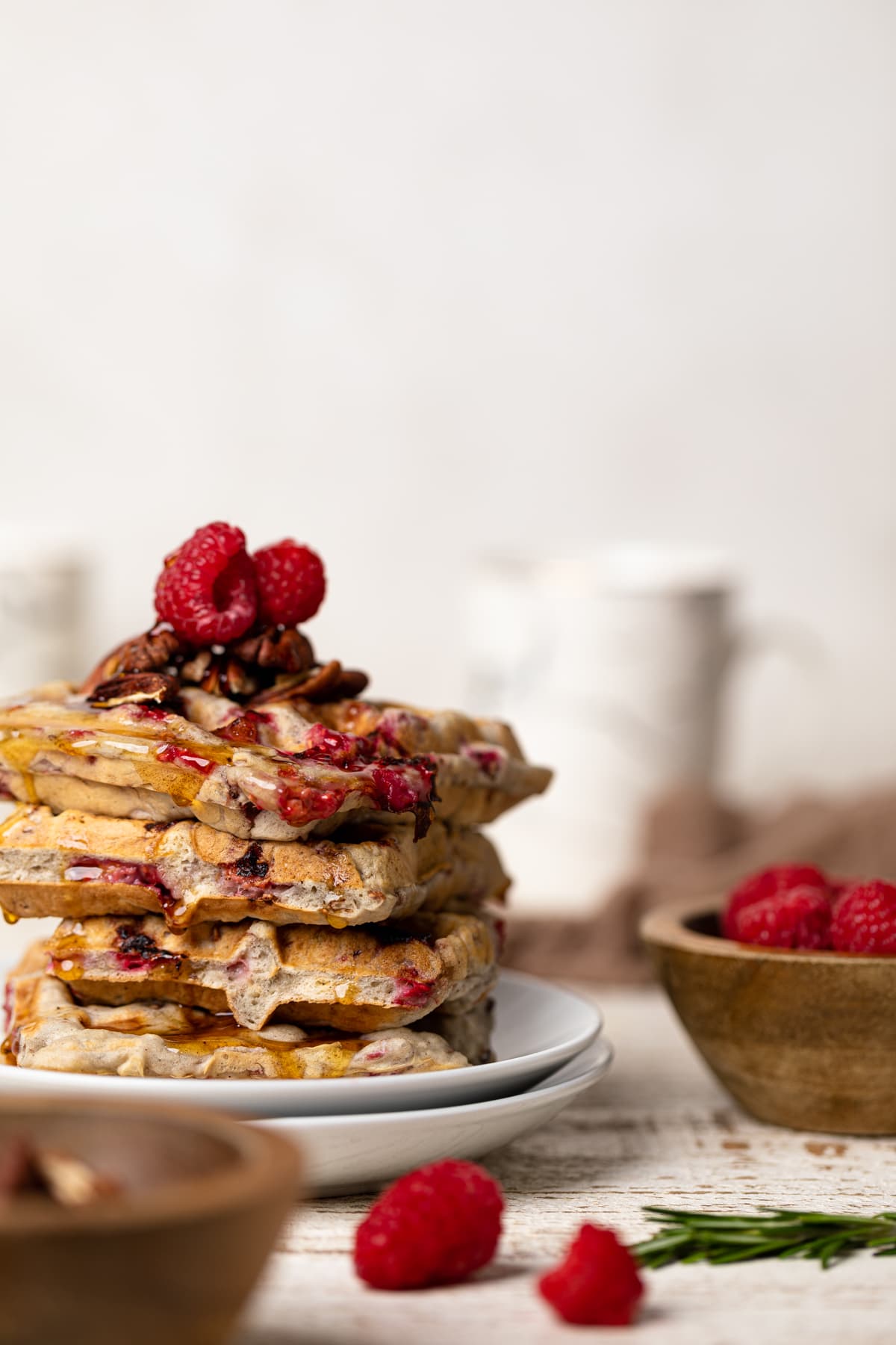 Stack of Raspberry Pecan Vegan Waffles next to a wooden bowl of raspberries