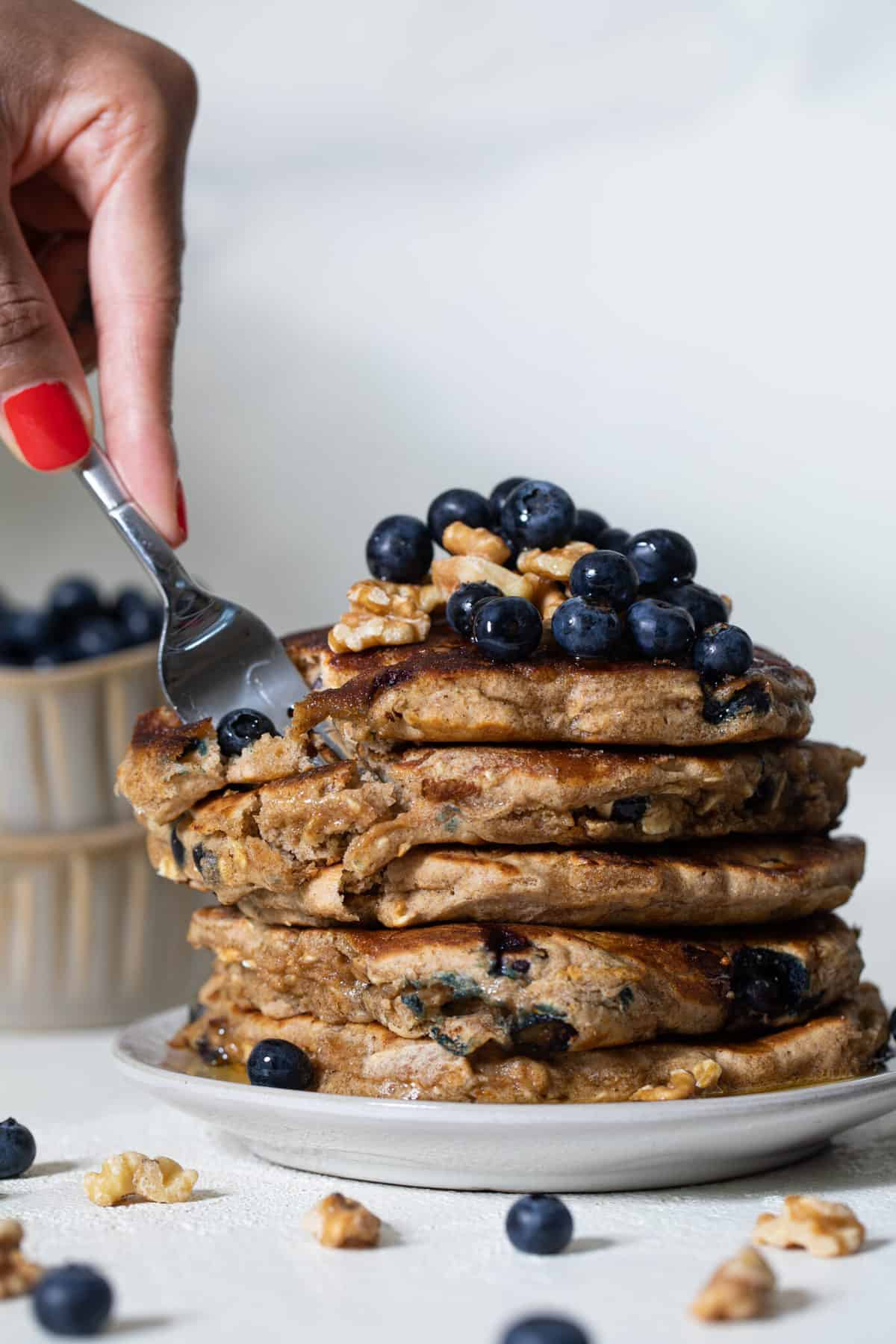 Woman using a fork to grab some Blueberry Whole Wheat Pancakes.