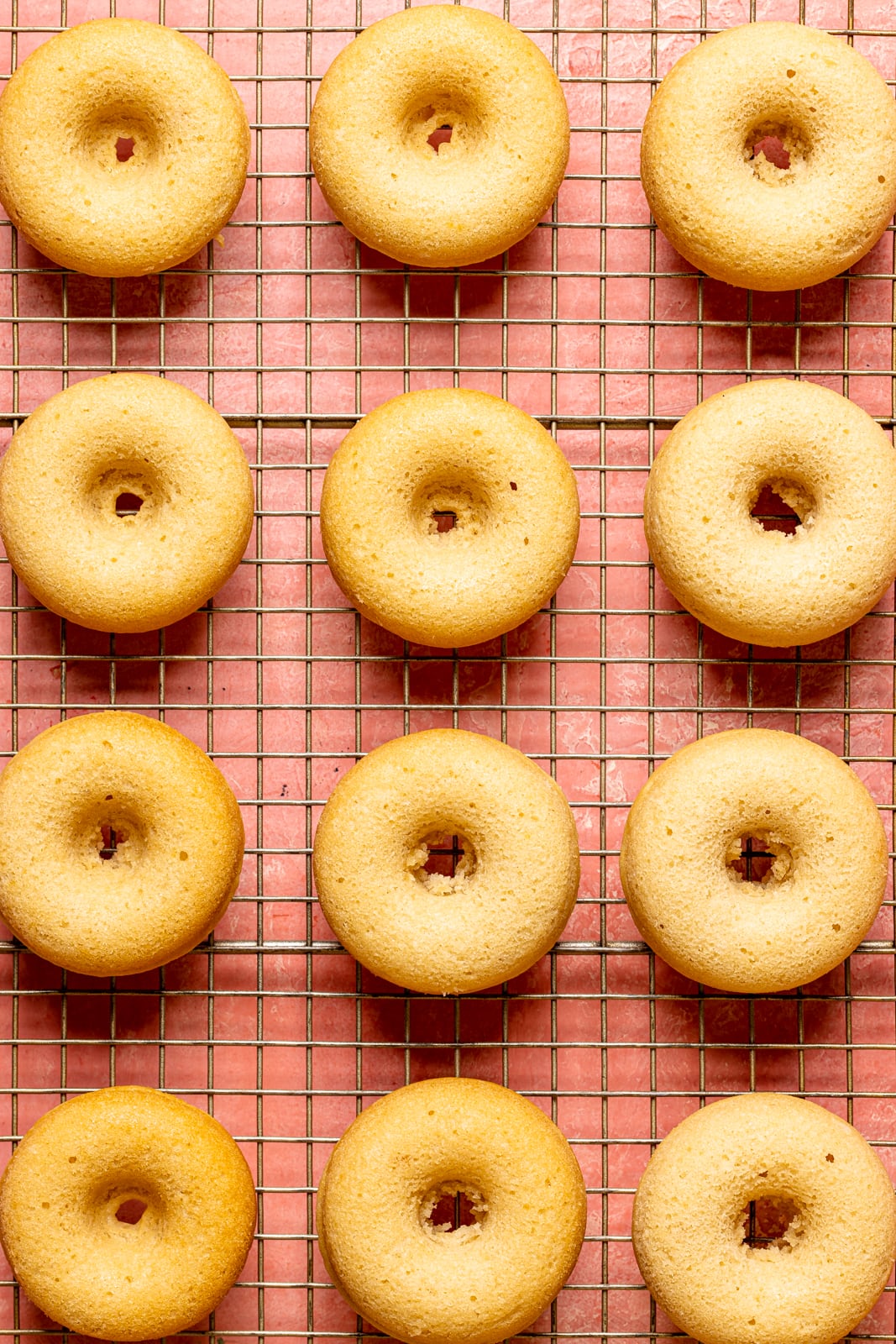 Baked donuts on a wire rack on a pink table.