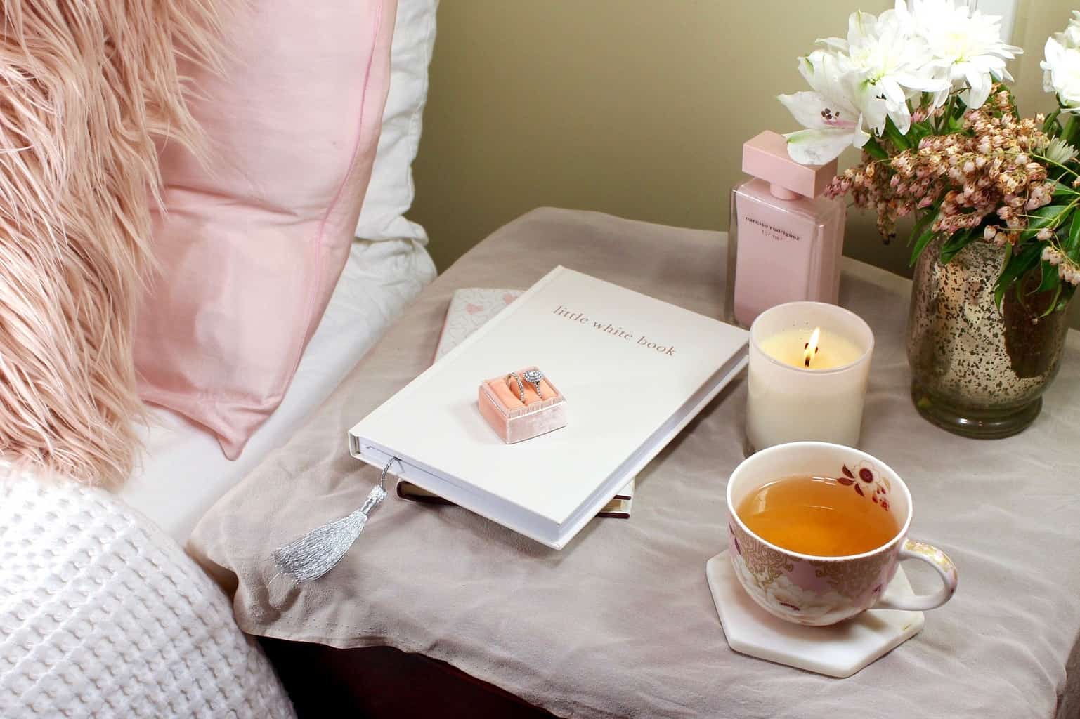 Rings on a \"little white book\" on a bedside table with a candle and mug.
