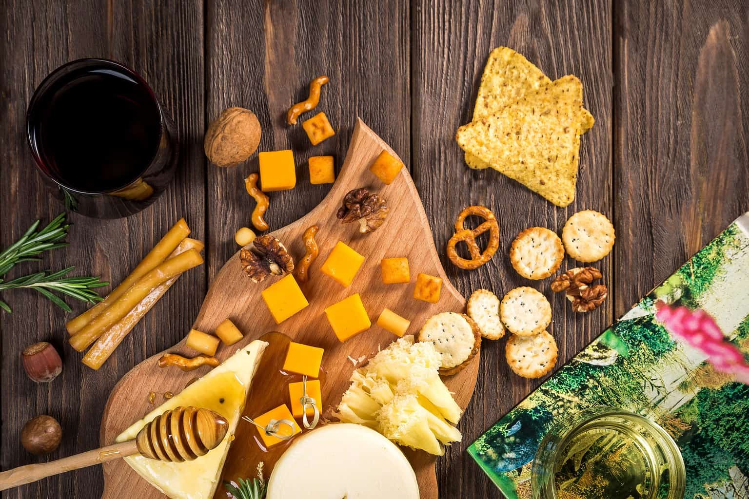 Cheese, crackers, honey, and other ingredients on and around a wooden board.