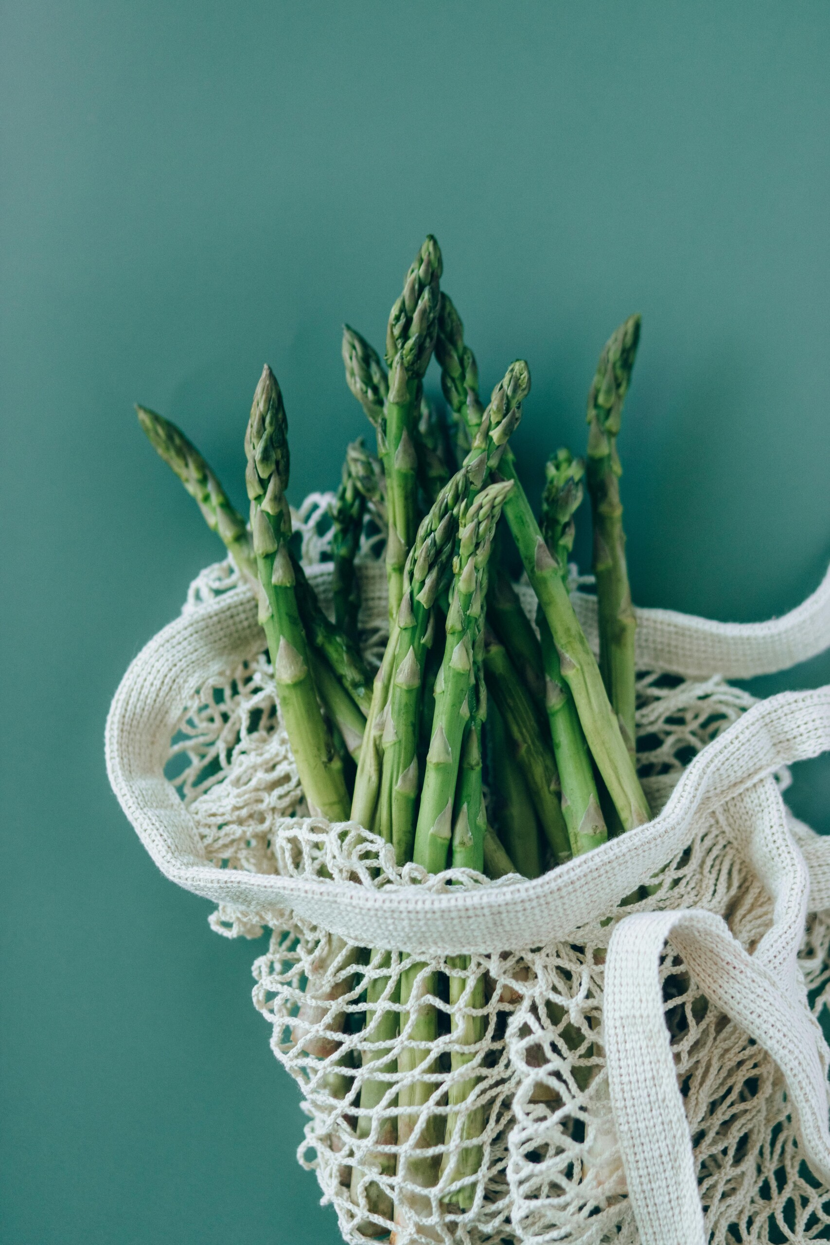 An image of asparagus in a grocery bag on a green background. 
