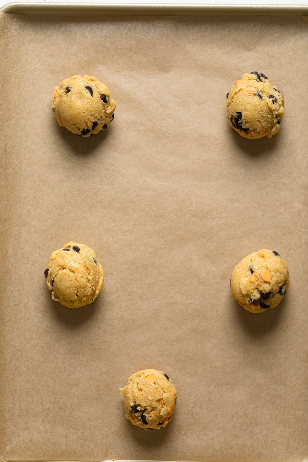 Balls of Crinkled Chocolate Chip Butterscotch Cookie dough on parchment paper