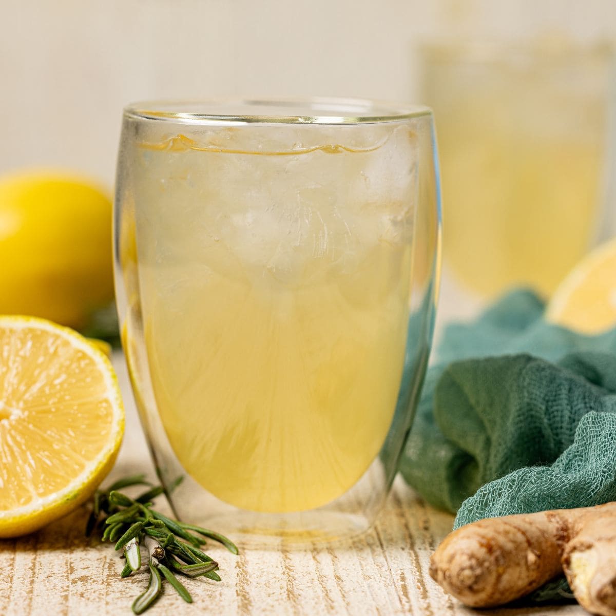 Two glasses of ginger ale with lemon, ginger root, and rosemary.