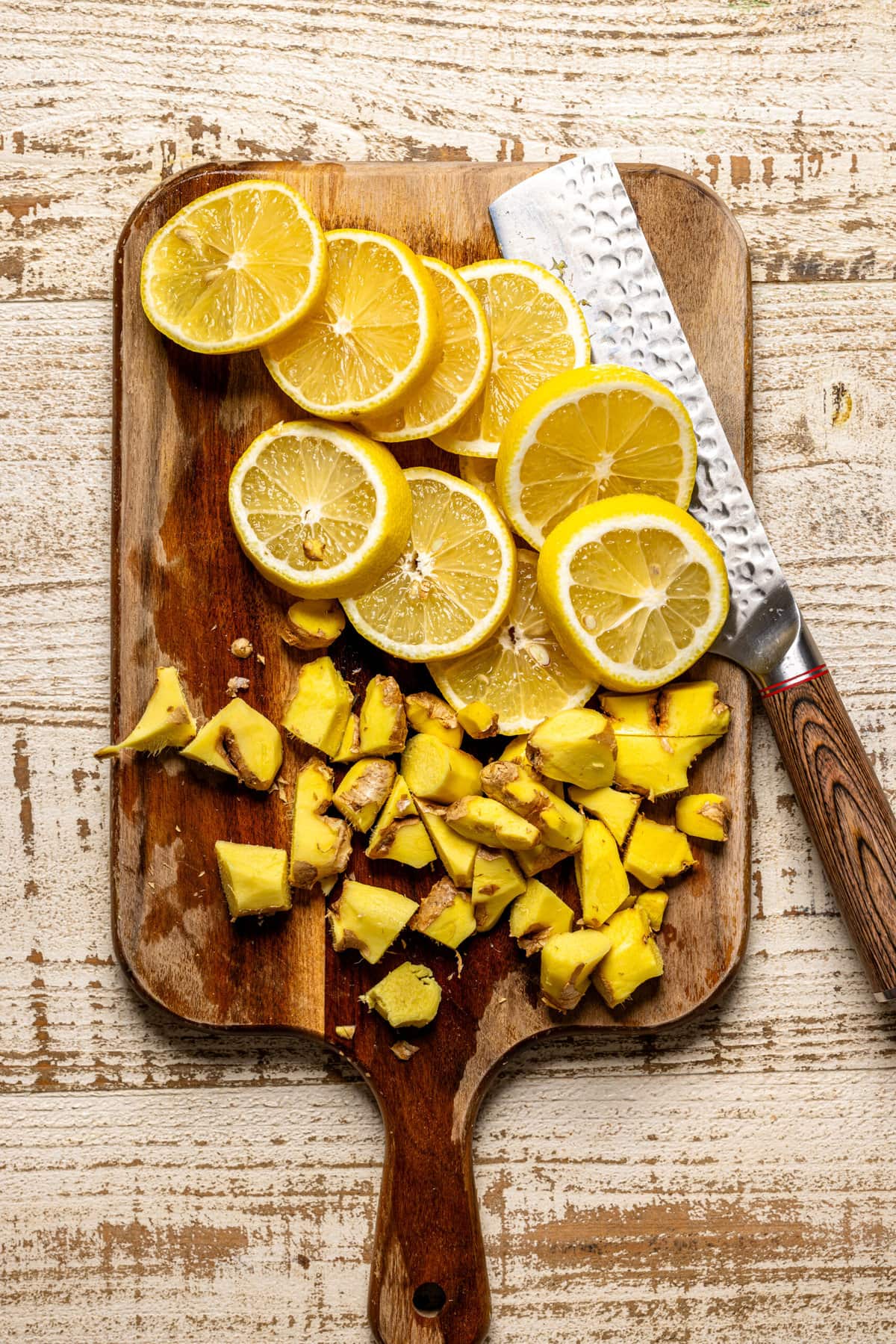 Lemon slices and ginger on a cutting board with a knife.