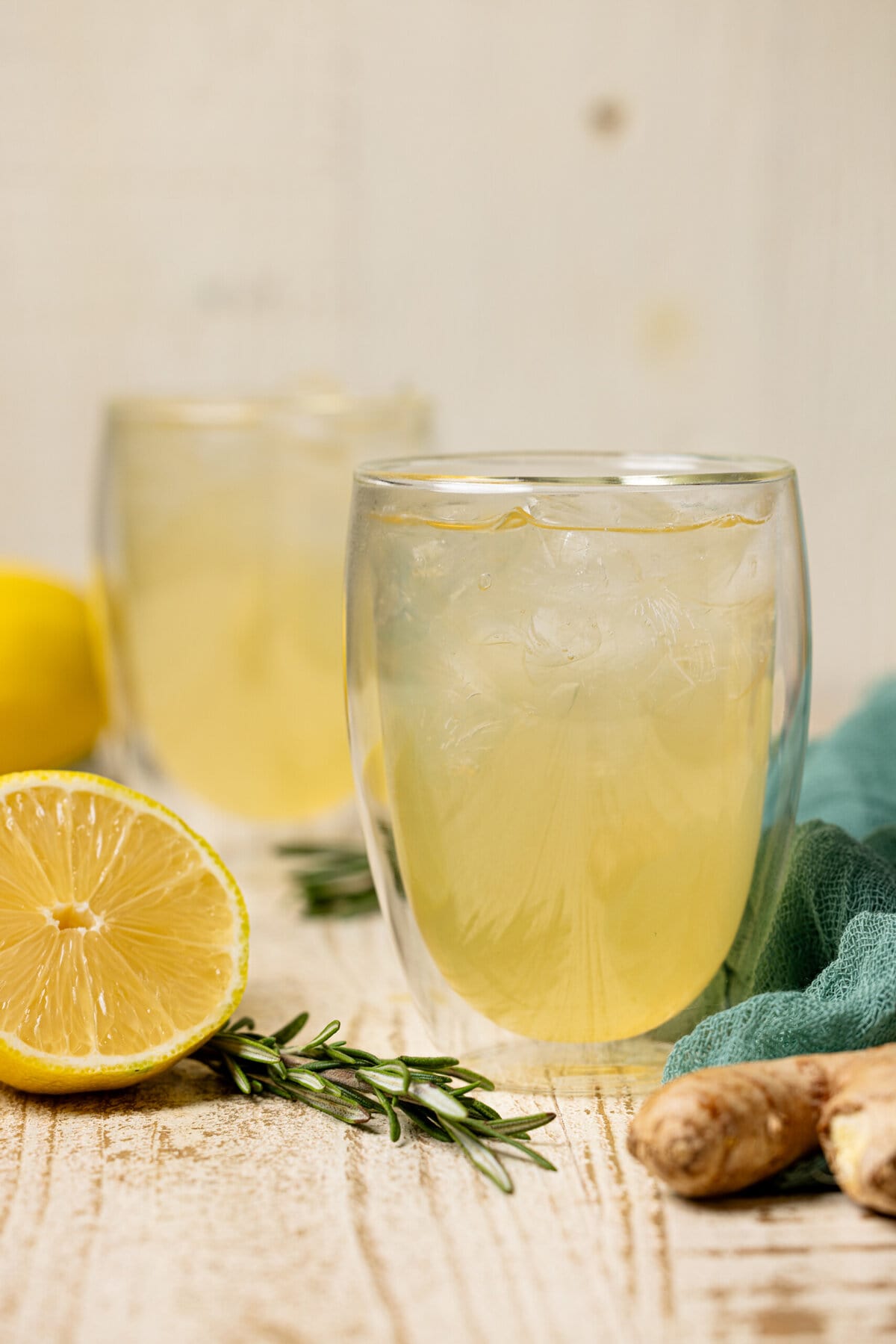 Ginger ale in a clear glass with lemon, ginger root, and rosemary.