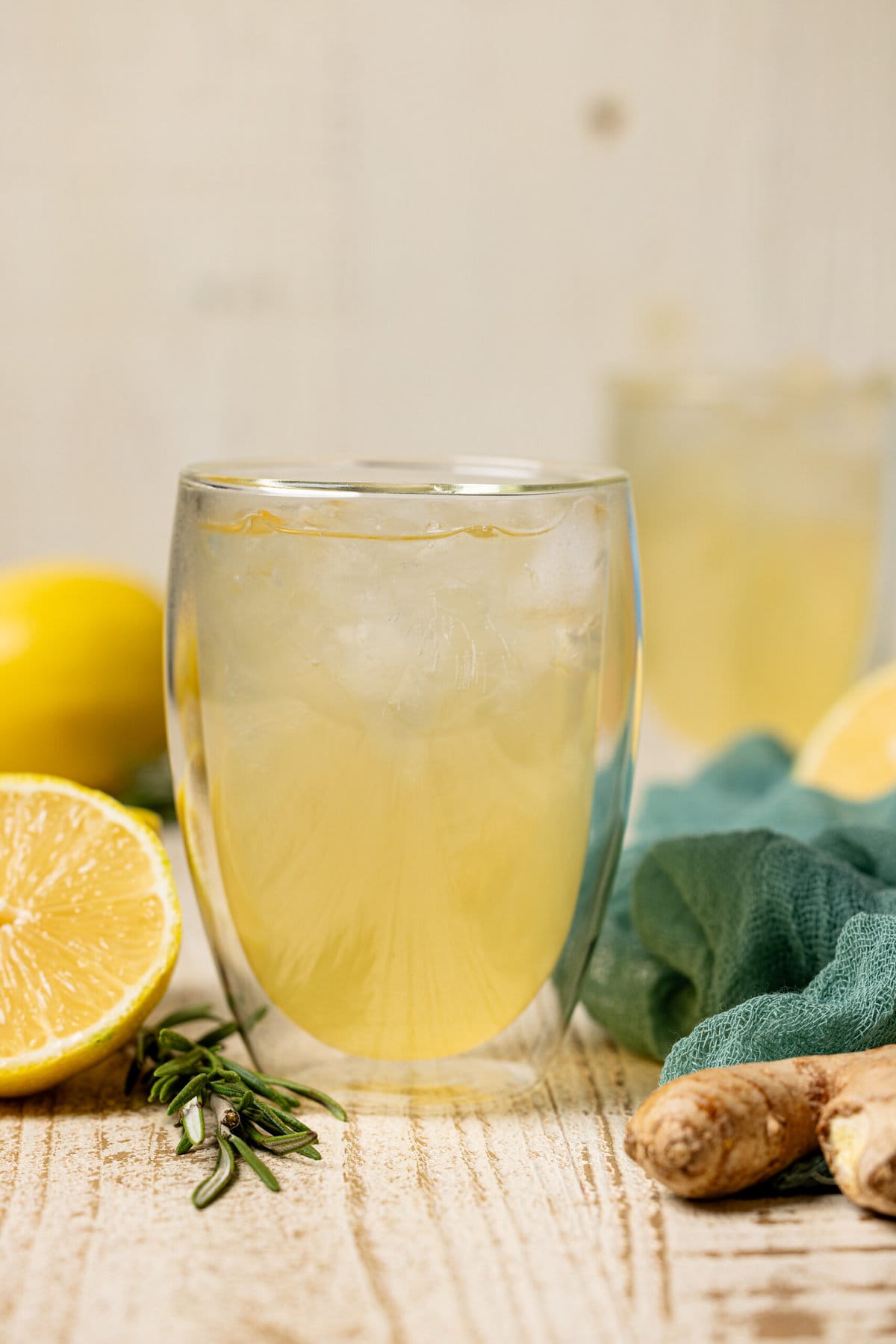 Two glasses of ginger ale with lemon, ginger root, and rosemary.