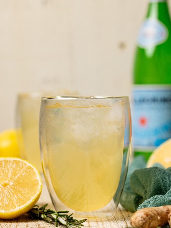 Up close glasses of ginger ale with a bottle of sparkling water and lemons.