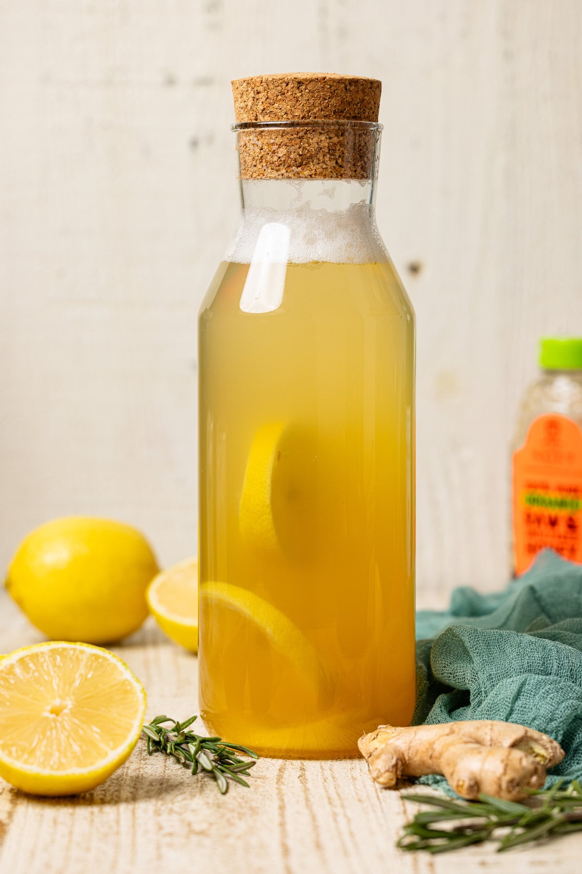 Ginger ale in a tall glass bottle with lemons and honey in the background. 