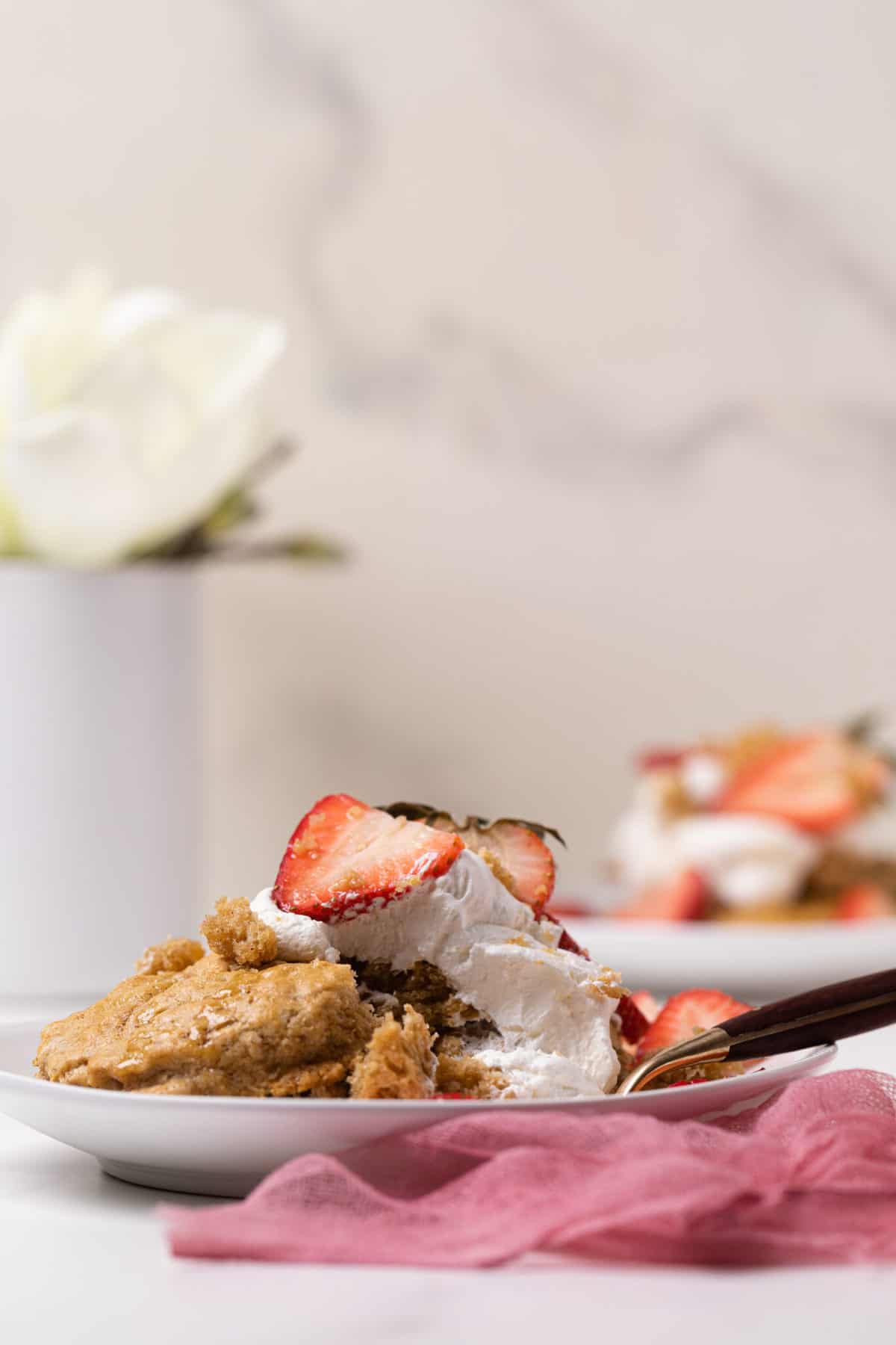 Maple Whole Wheat Oatmeal Strawberry Shortcake on a white plate with a white flour in the background and pink gauze