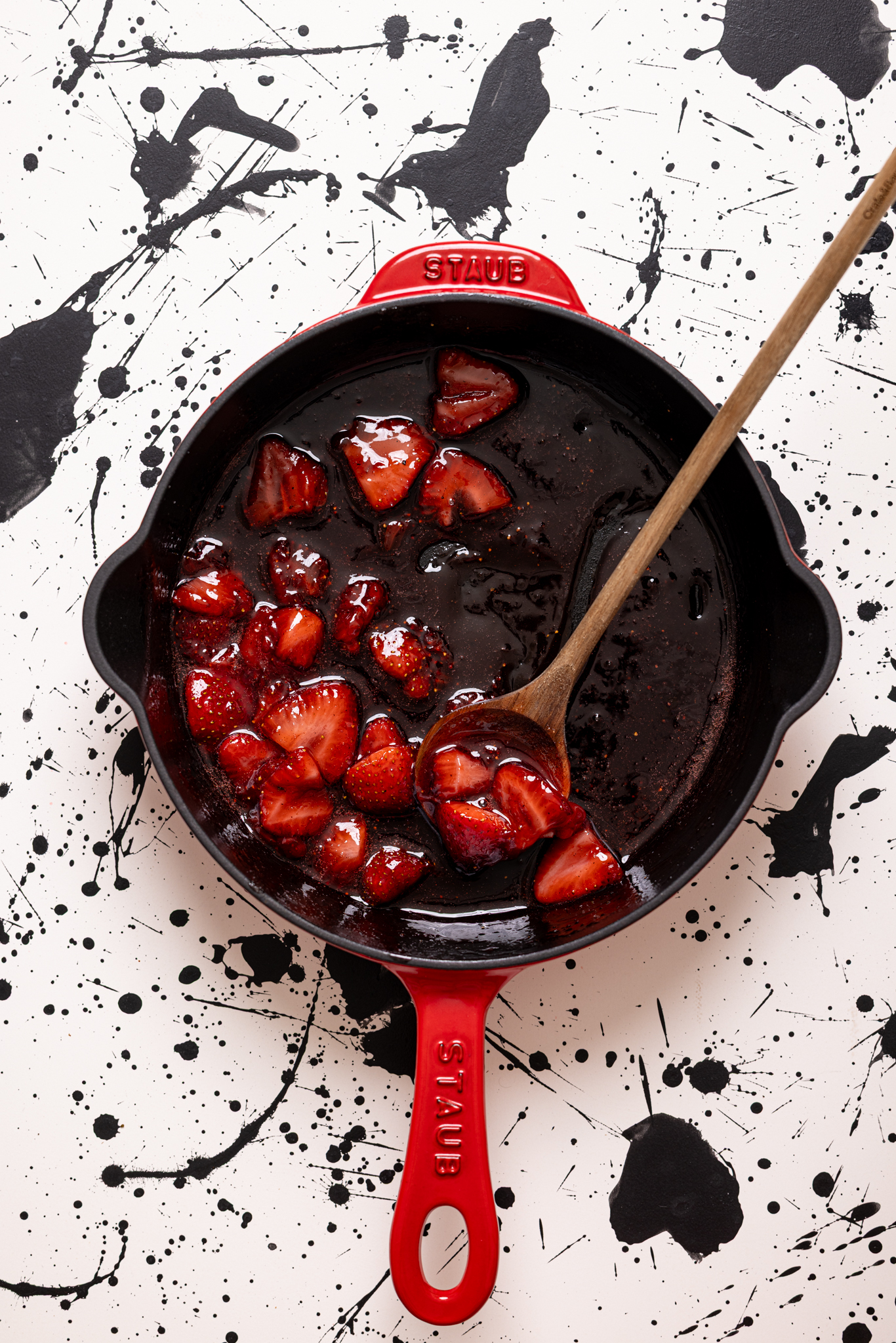 Strawberry sauce in a red skillet with a wooden spoon.