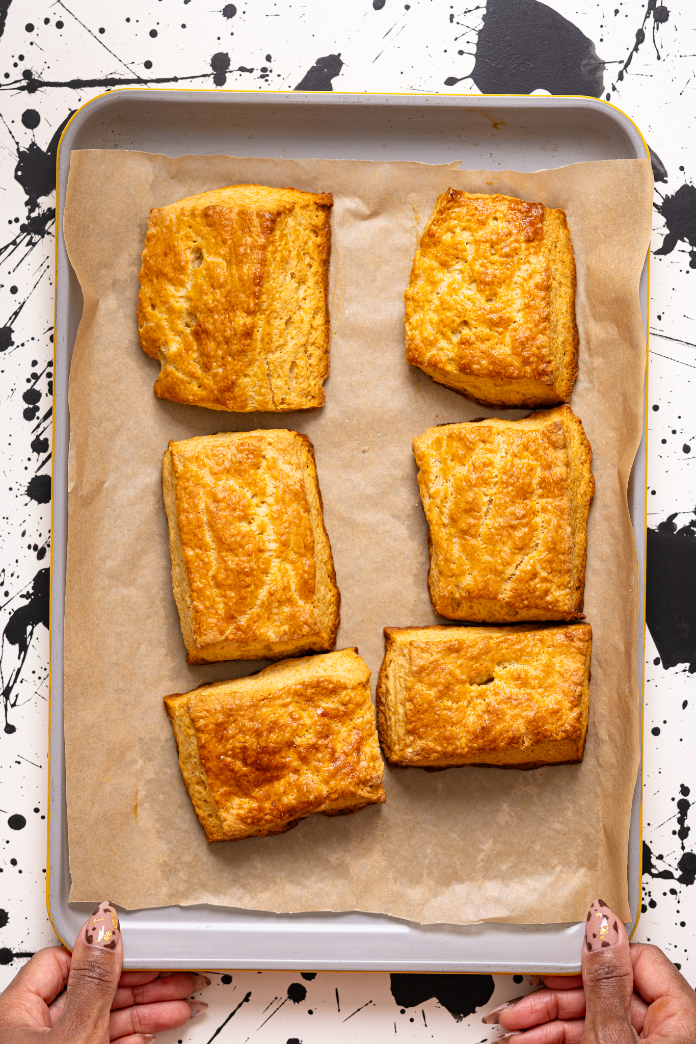 Baked flaky biscuits on a baking sheet with parchment paper held by woman hands.