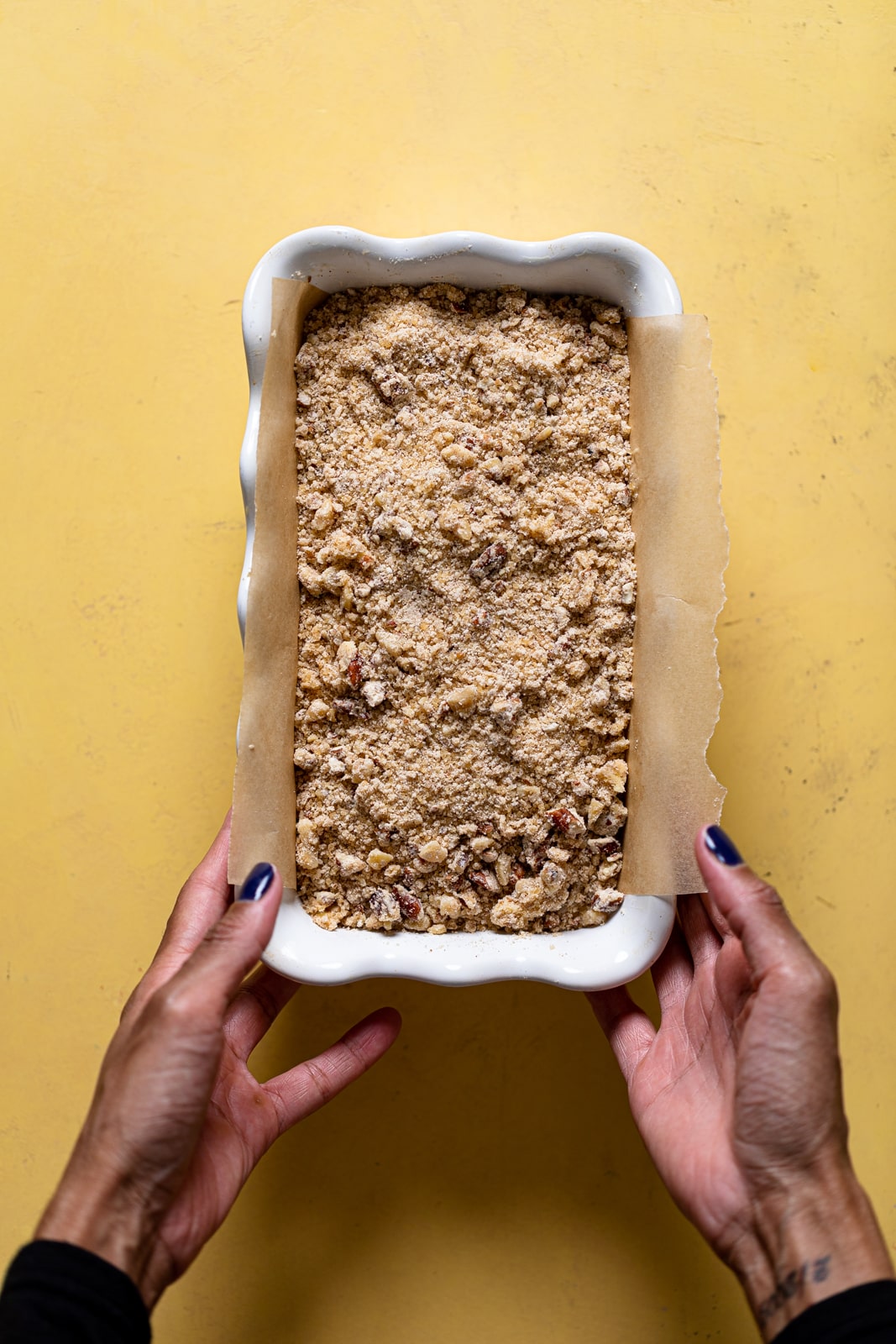 Hands holding a bread pan with Vegan Cinnamon Crunch Banana Bread