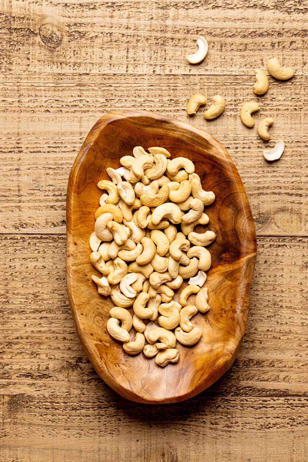 Cashews in a brown bowl on a brown wood table. 