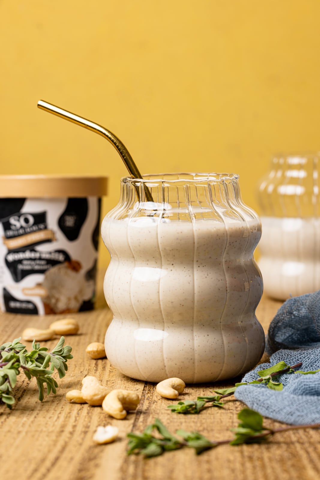 Drinks in two cups with a straw on brown wood table with an ice cream carton and cashews.