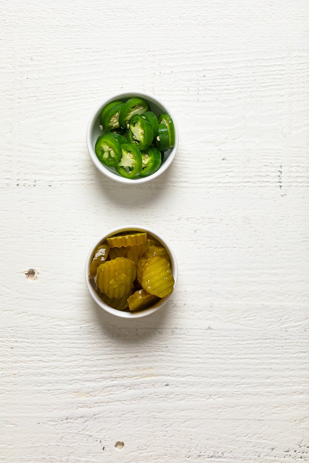 Small bowls of pickle slices and hot pepper slices