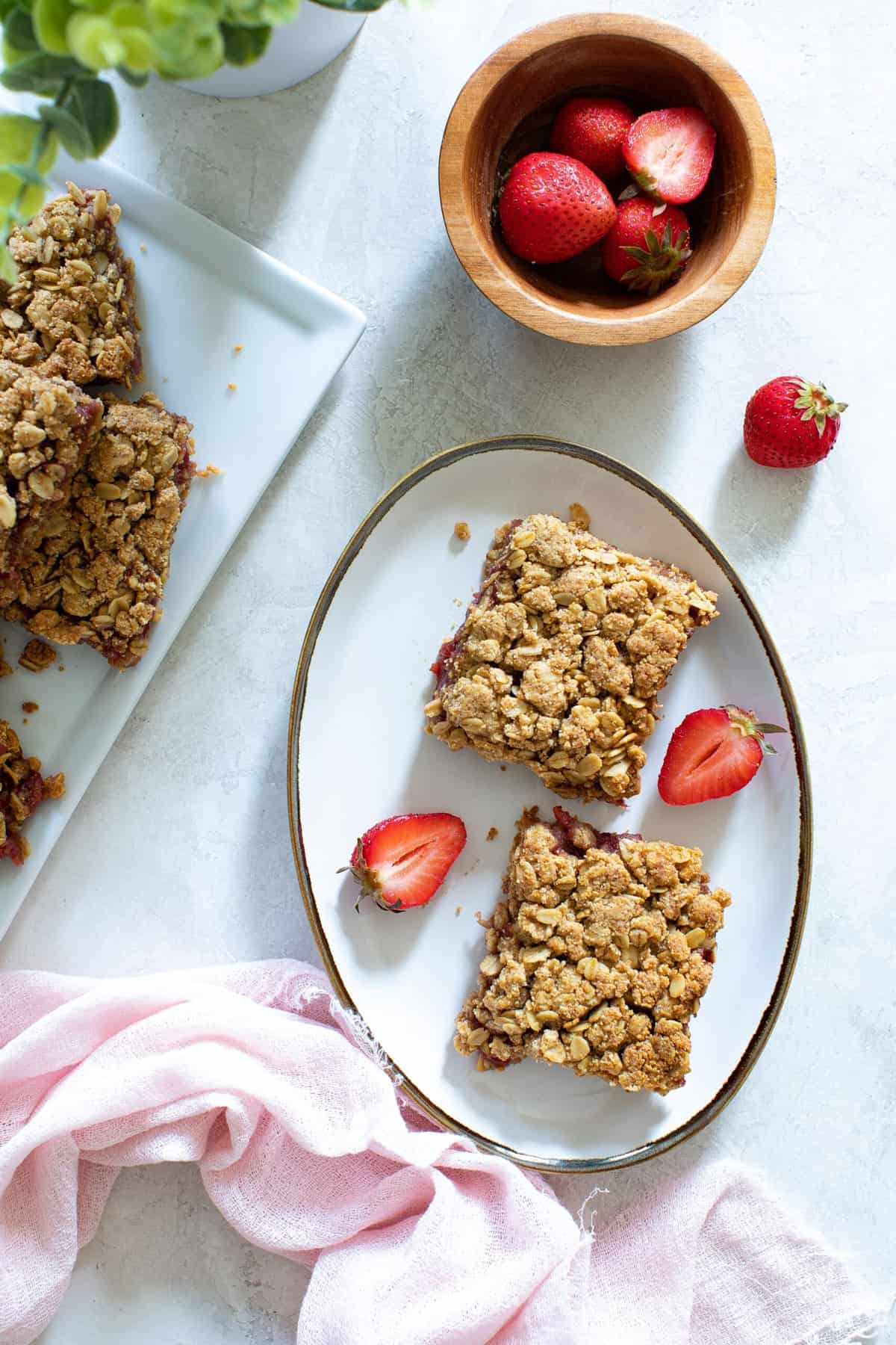 Vegan Strawberry Peanut Butter Oatmeal Bars on a gold-rimmed plate with halved strawberries.