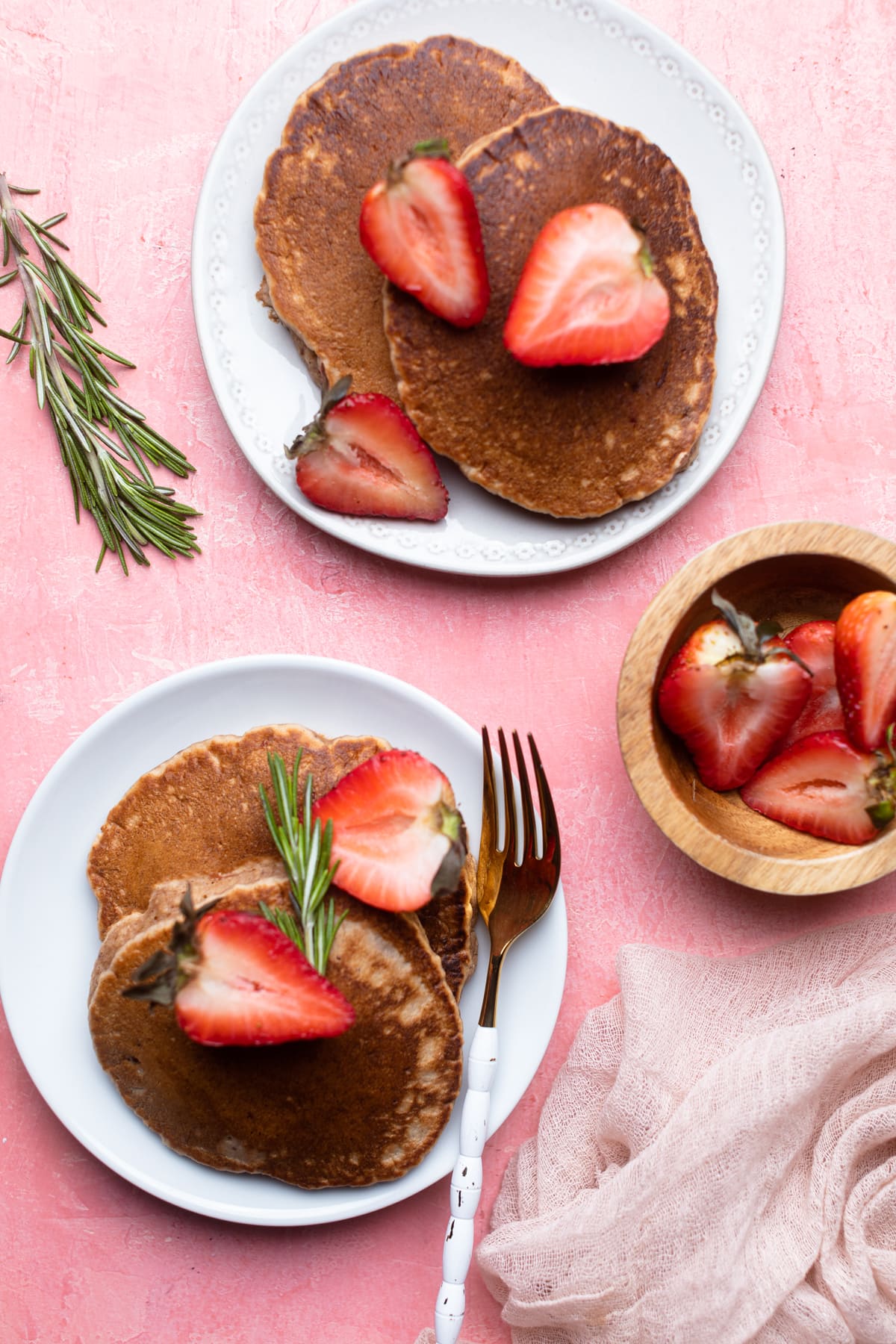 Plates of Whole Wheat Strawberry Pancakes and halved strawberries.