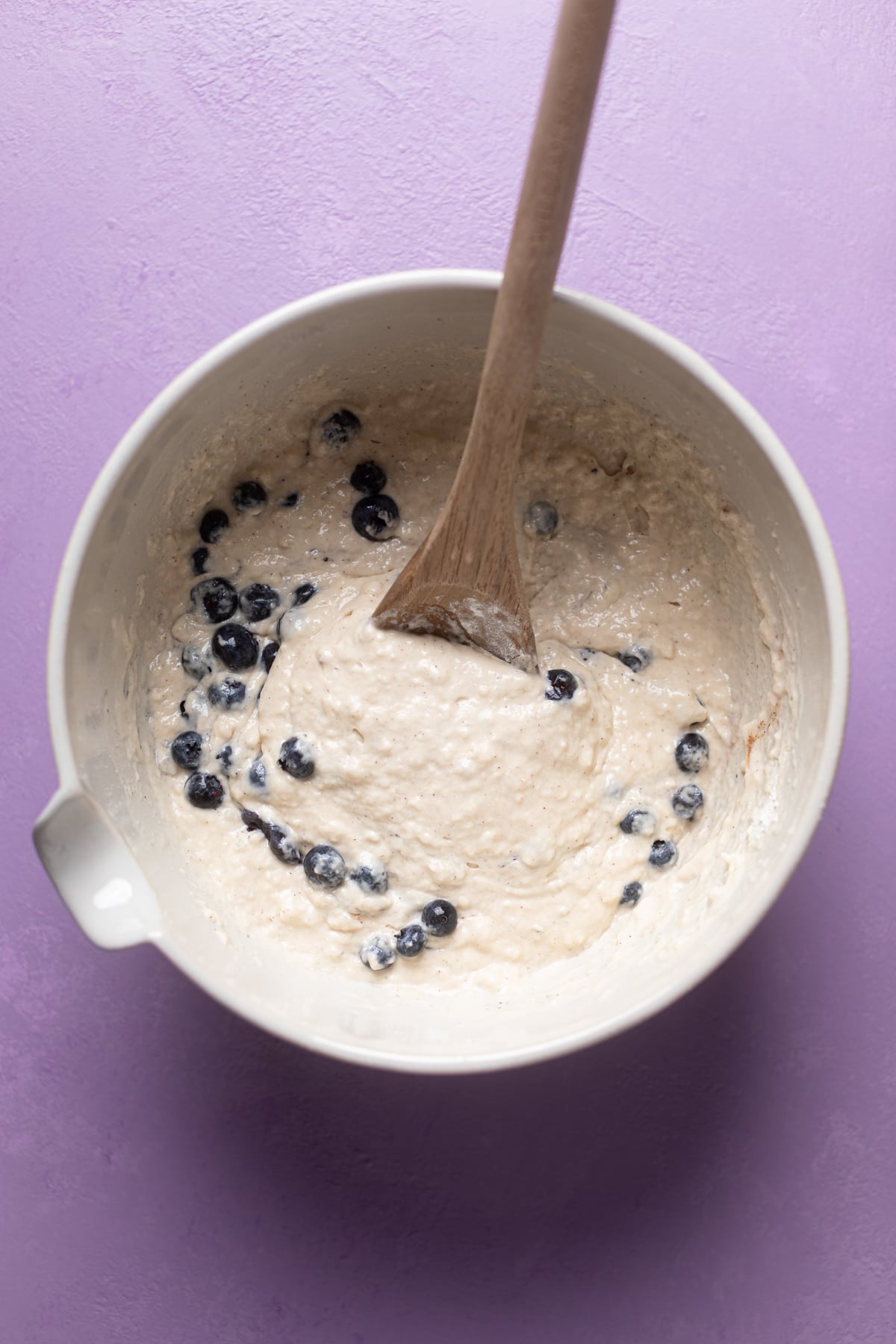 Overhead shot of Dairy-Free Almond Blueberry Pancake batter in a bowl with a wooden spoon