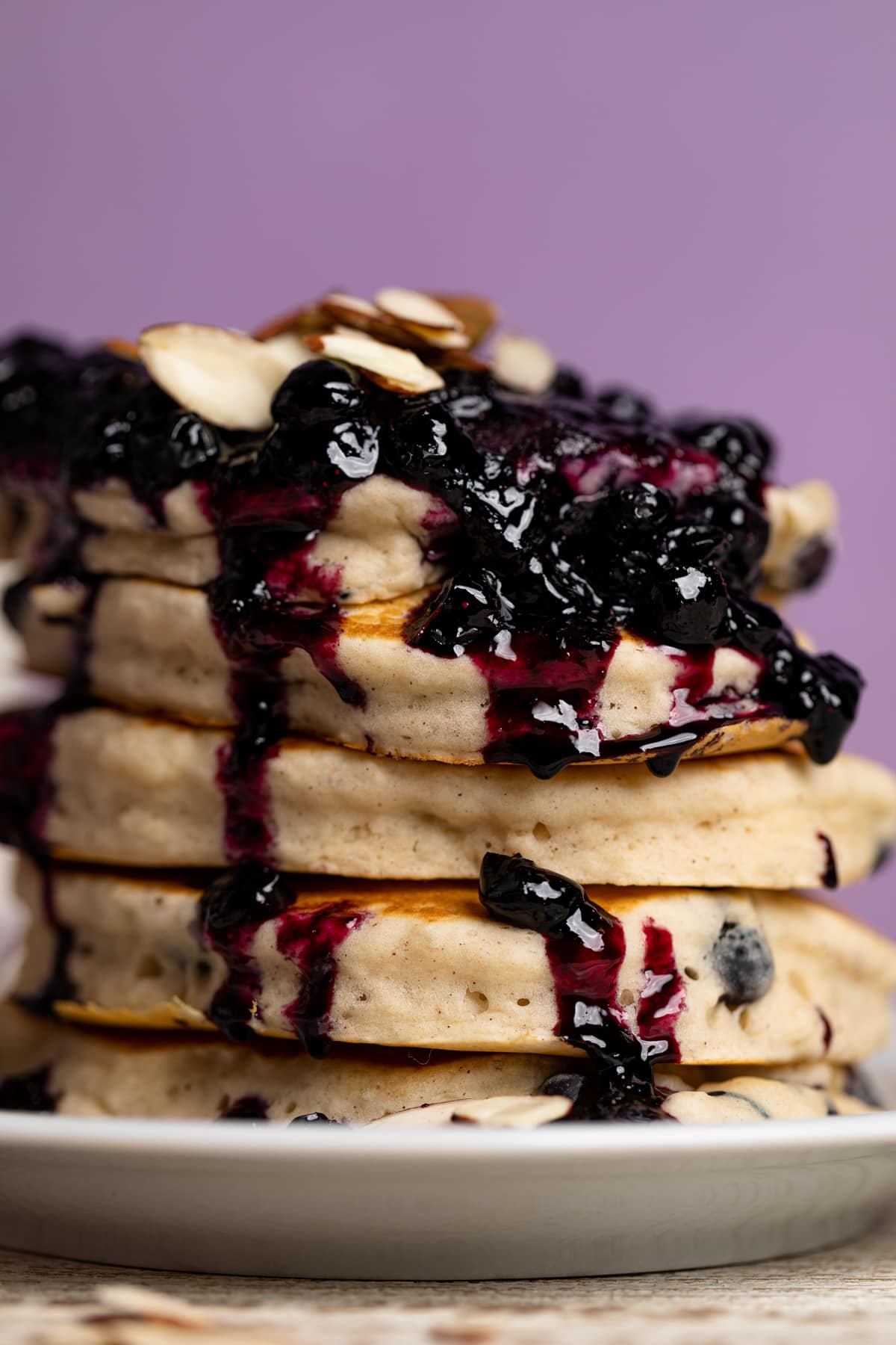 Closeup of a stack of Dairy-Free Almond Blueberry Pancakes dripping with blueberry topping