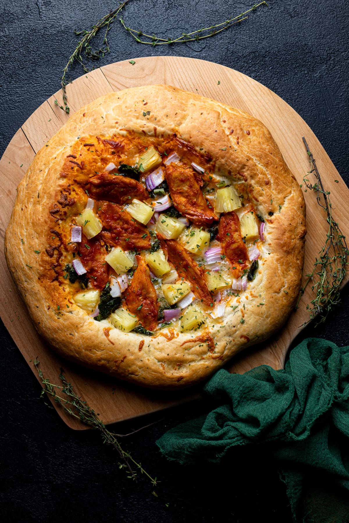 Wooden board topped with a Plant-based Hawaiian Buffalo \'Chicken\' Pizza.