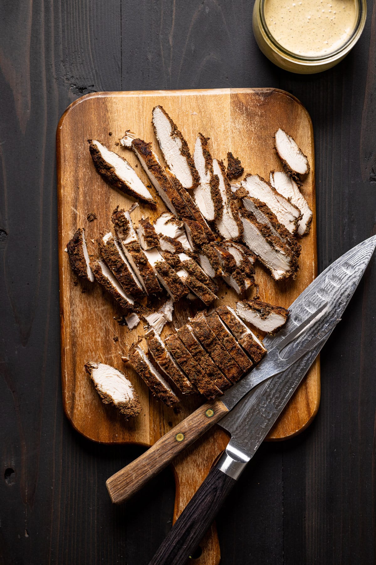 Sliced jerk chicken on a cutting board with a knife and two-pronged fork