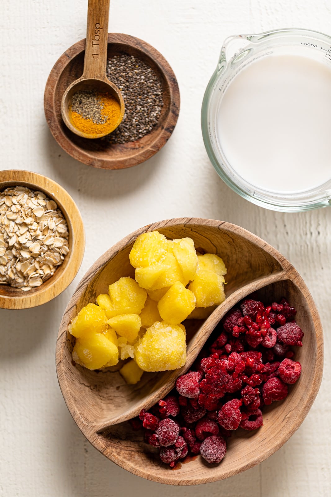 Bowls of ingredients including frozen mango, frozen raspberry, and oats.