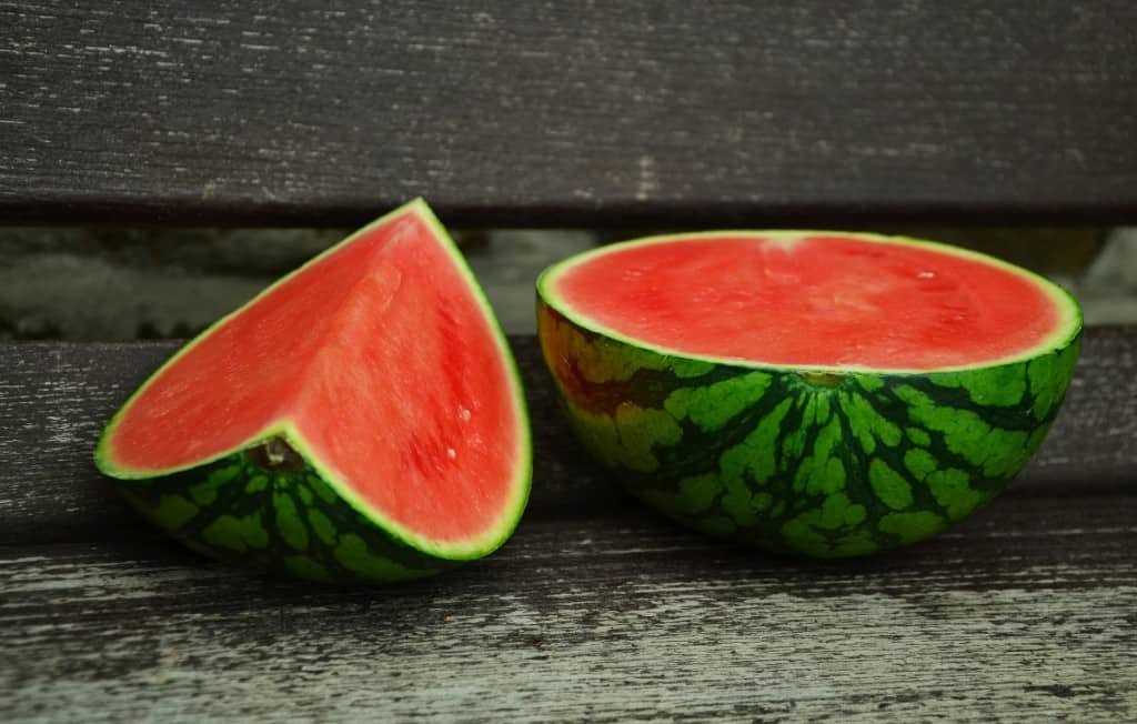 Half of a watermelon next to a quarter of a watermelon.