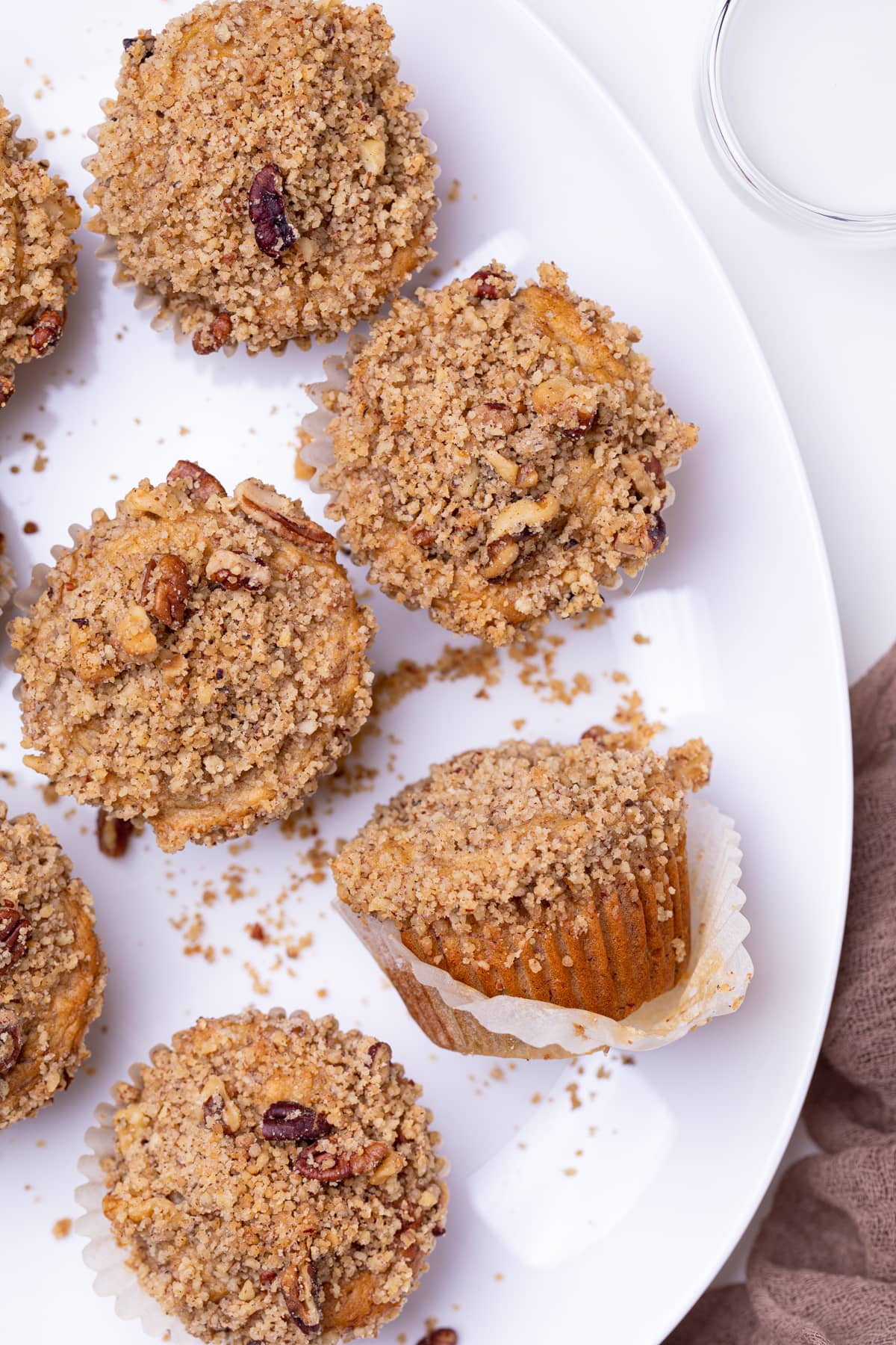 Vegan Banana Muffins with cinnamon streusel on a white plate, one of which is lying down.