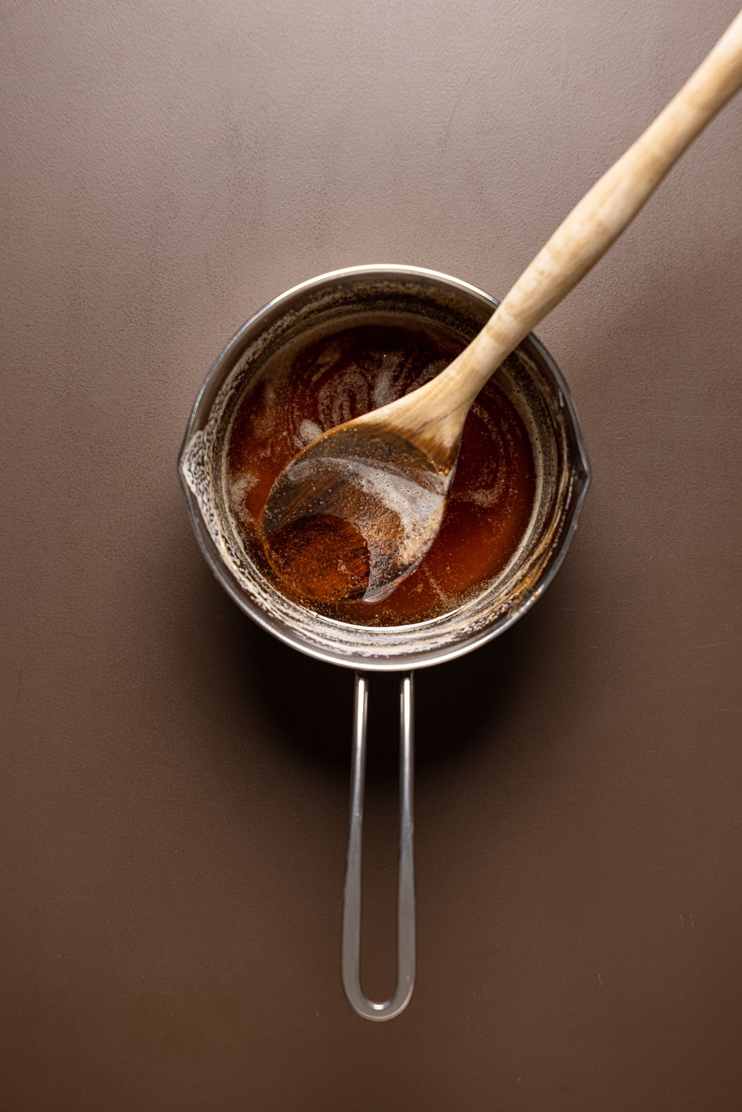 Melted brown butter in a saucepan with a wooden spoon on a brown table.