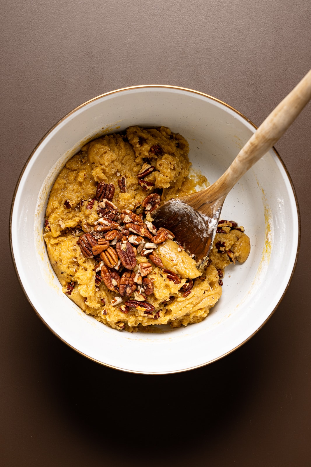 Cookie dough in a white bowl with a wooden spoon on a brown table.