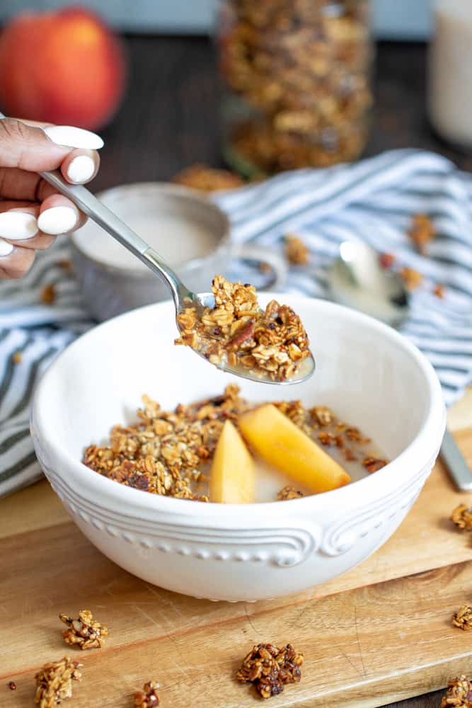 Spoon scooping Caramelized Peach Cinnamon Breakfast Granola from a bowl.