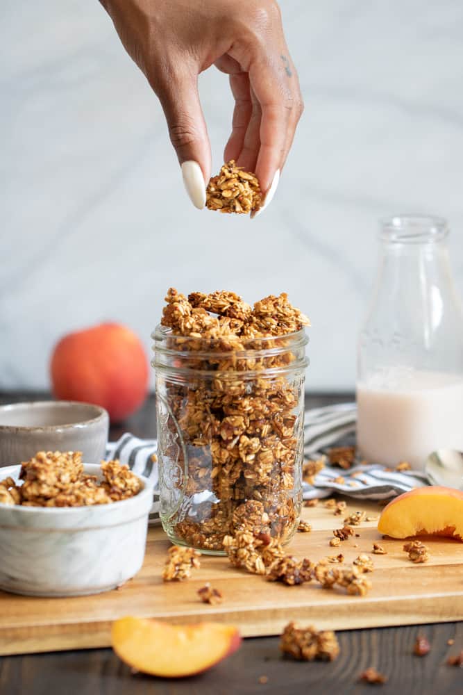 Woman grabbing a piece of Caramelized Peach Cinnamon Homemade Breakfast Granola from a jar.