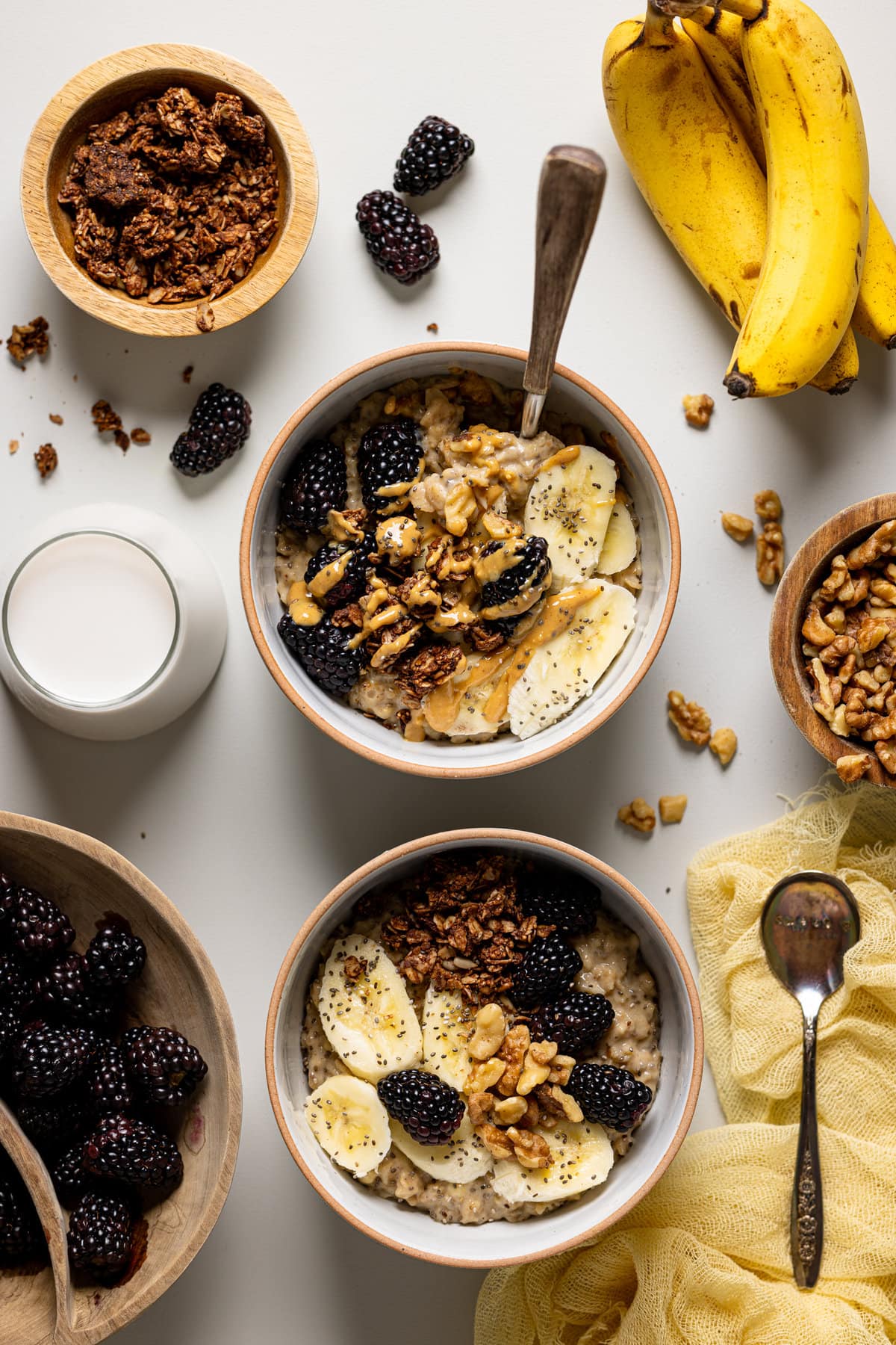 Two bowls of Protein Peanut Butter Banana Chia Oatmeal surrounded by various toppings