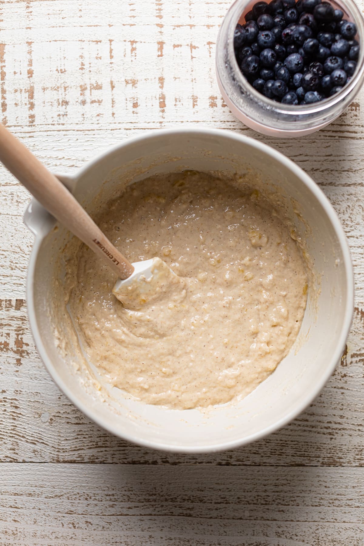 Bowl of Vegan Banana Blueberry Pecan Crumble Muffin batter next to a jar of blueberries