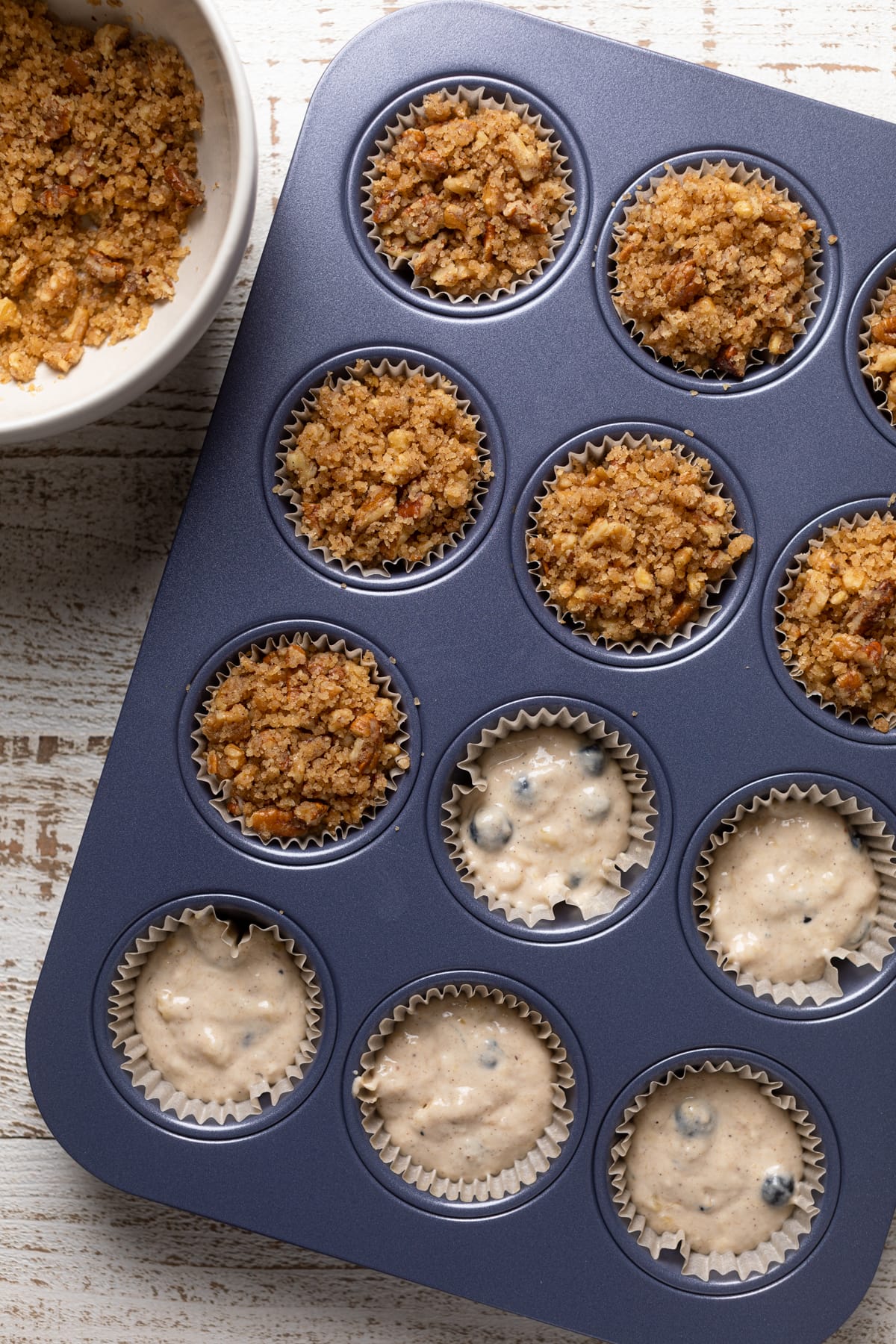 Vegan Banana Blueberry Pecan Crumble Muffin batter in a muffin pan, some of which have been topped with crumble