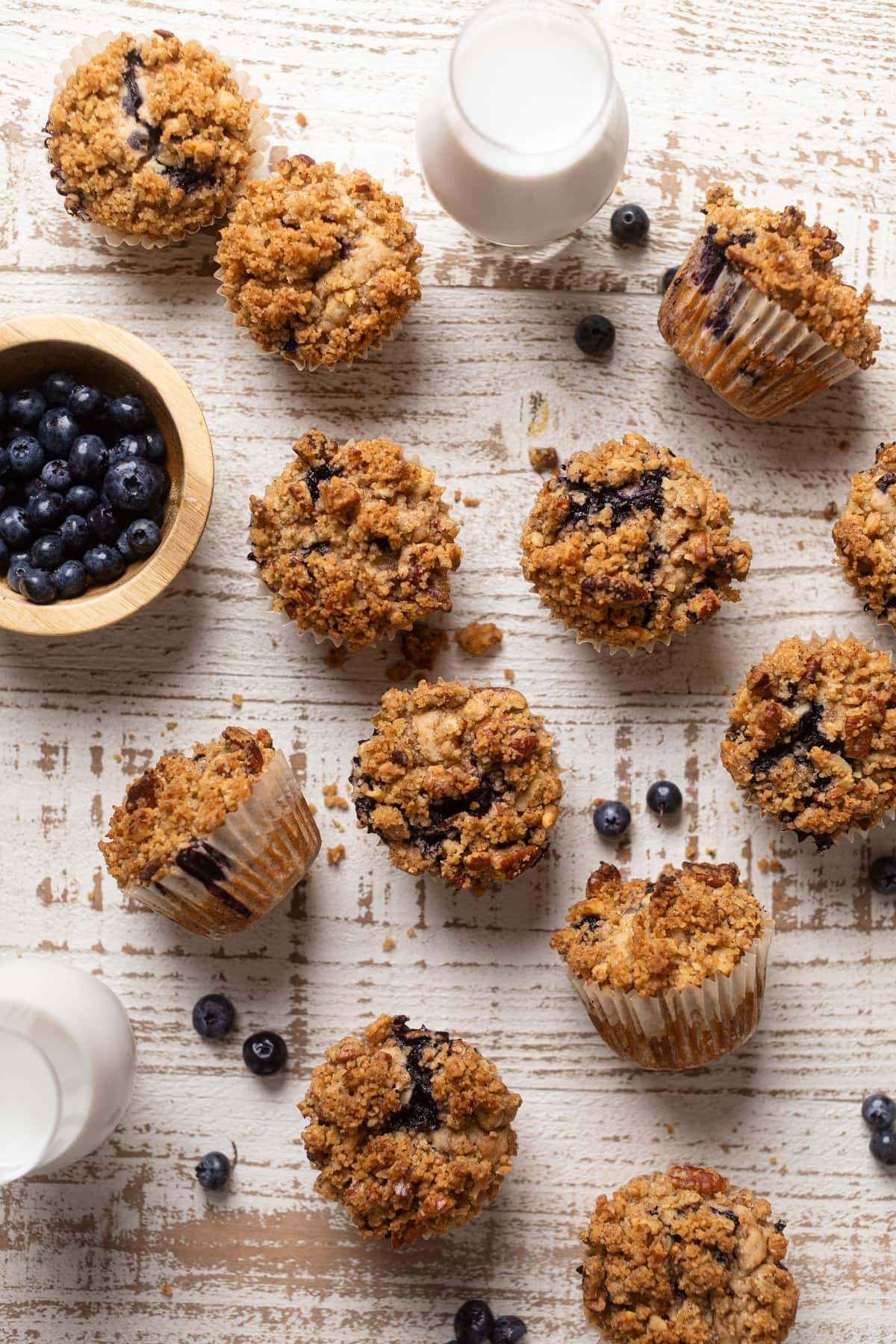 Vegan Banana Blueberry Pecan Crumble Muffins on a white table with a bowl of blueberries