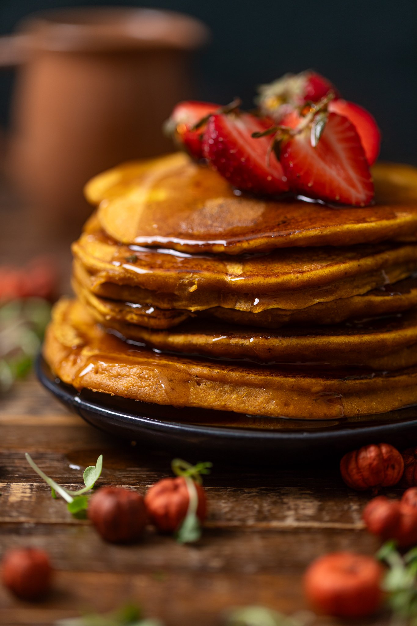 Up close shot of stack of Cozy Pumpkin Spice Pancakes with strawberries and syrup.