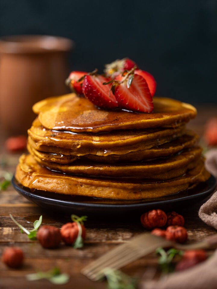 Stack of Cozy Pumpkin Spice Pancakes on a black plate with toppings and syrup.