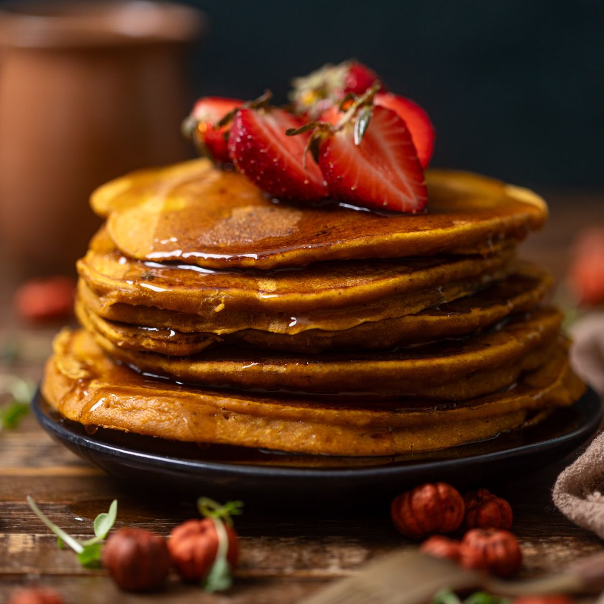 Stack of Cozy Pumpkin Spice Pancakes on a black plate with toppings and syrup.